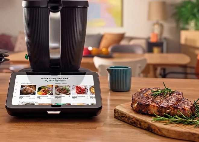 Urządzenie Thermomix z ekranem wyświetlającym przepisy na steki, a obok grillowany stek ribeye.